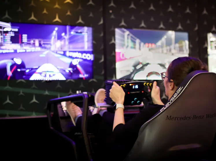 Visitor using a high-tech racing simulator at Mercedes-Benz World, engaging in a virtual Formula 1 driving experience with immersive screens and controls.